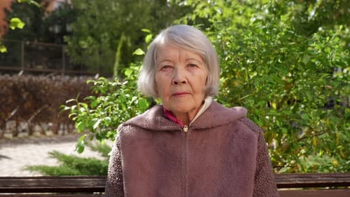 A Grandmother with Gray Hair and a Wrinkled Face in a Park on a Bench