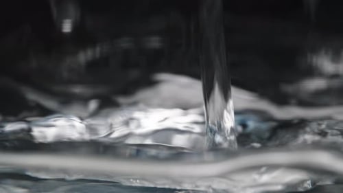 A stream of Water pours into a container, creating ripples and bubbles on the surface, captured in
