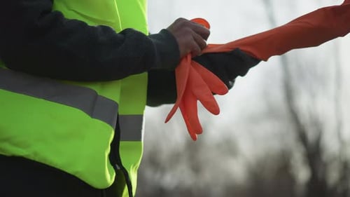 Construction Worker Puts on Protective Orange Gloves
