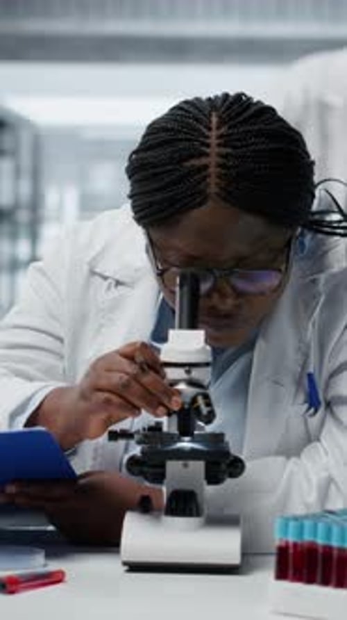 Woman uses microscope in laboratory with test tubes