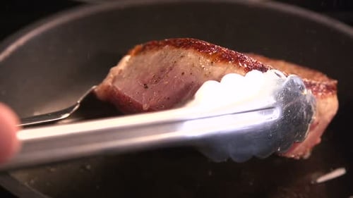 Chef expertly flipping sizzling beef steak fillet in restaurant kitchen close up