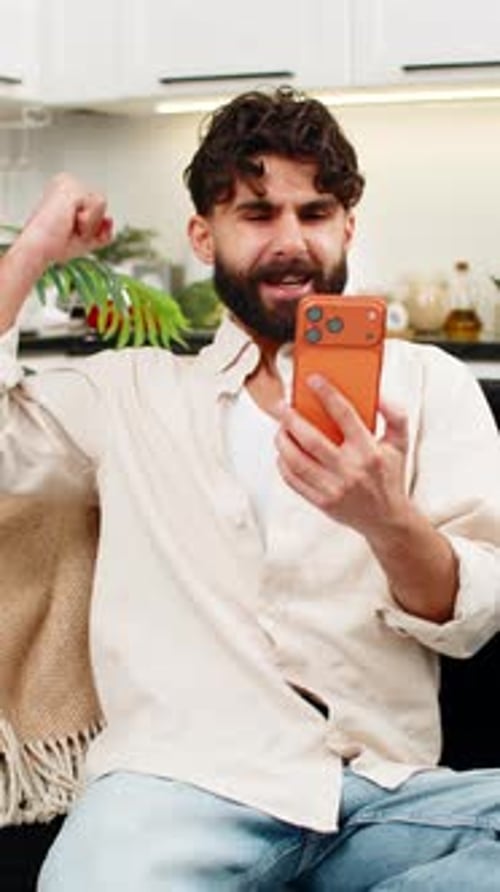 Man Using Phone at Home Reacts with Excitement