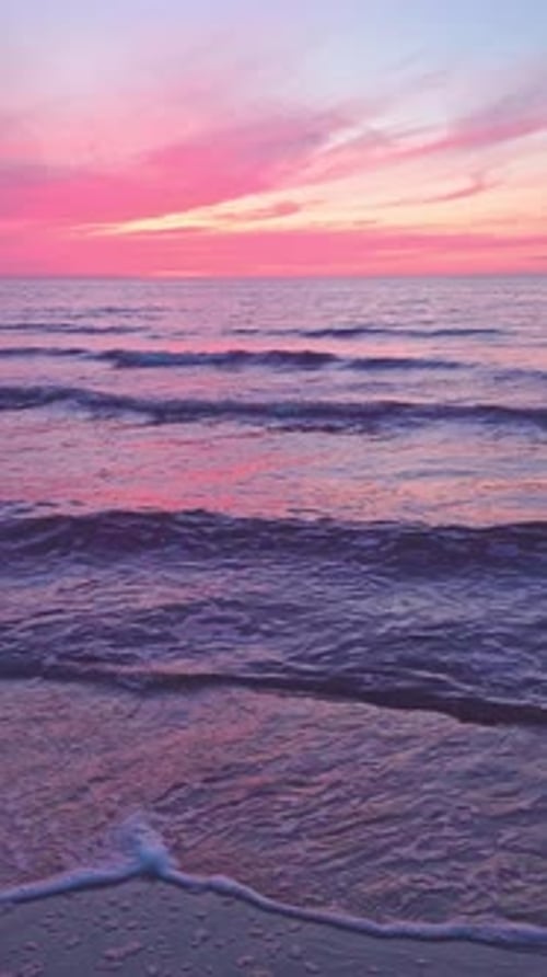 Vertical video 4K tranquil landscape of sunset pink sky, small sea waves, evening beach