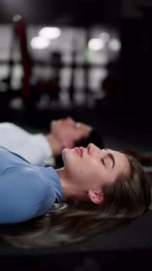Content Woman in Gym Lying Down Relaxed Postexercise with a Companion in a Focused State