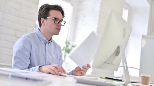 Working Young Man Reading Documents and using Laptop in Office