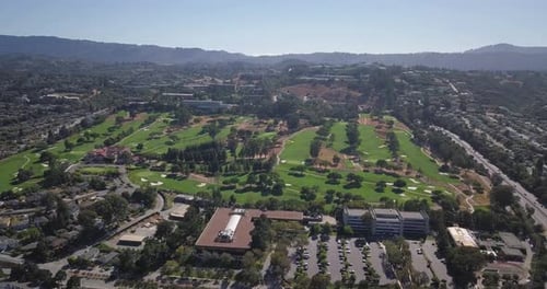 Aerial helicopter shot of golf course field with mountains in background on a sunny day with clear b