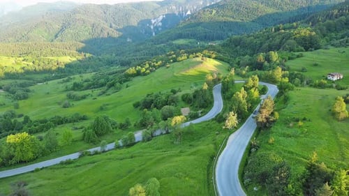 A Road Passes Hills Covered with Spruce Forests and Meadows Against a Cloudy Sky