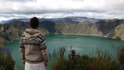 hombre latino mirando de lejos mira la majestuosa laguna azul del volcán Quilotoa (3.914 m)