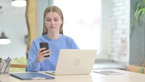 Woman Using Smartphone at Desk with Laptop