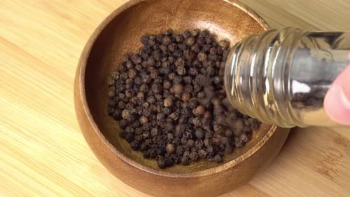 Pouring Black Peppercorns into Wooden Bowl