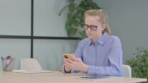 Woman Using Phone at Desk with Tablet and Papers