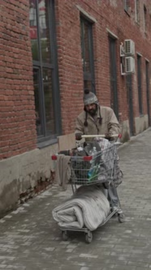 Man Pushes Shopping Cart along Urban Brick Building