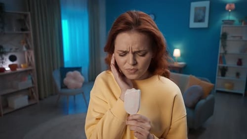 A Woman Eating Ice Cream Popsicle While Standing in the Living Room The Woman Grabs Her Cheek with a