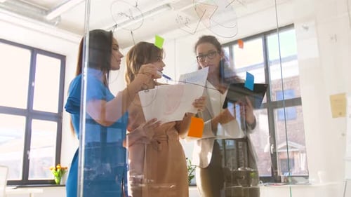 Women Collaborating on Glass Whiteboard in Modern Office
