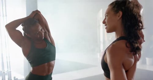 Stretching and chatting, two women in gym wearing athletic wear, staying fit