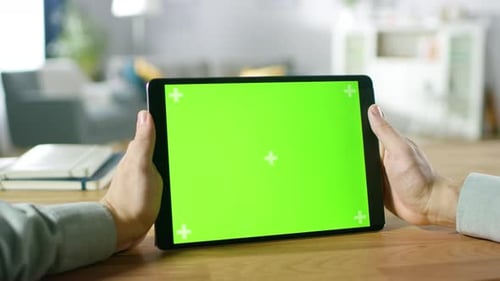 Mann, der einen digitalen Tablet-Computer mit grünem Modellbildschirm in der Hand hält und beobachtet, während er am Schreibtisch sitzt. Ma