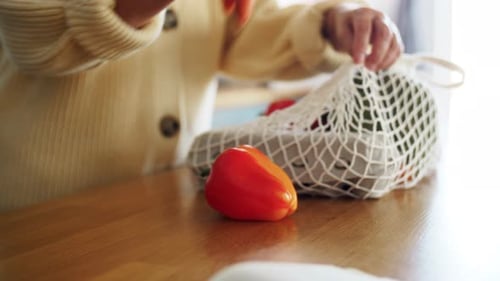 Manos de una mujer mayor desempacando verduras frescas en una bolsa de hilo en casa