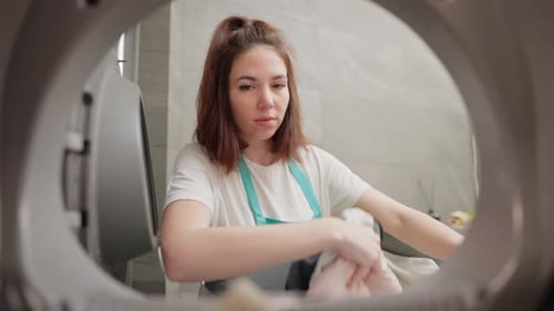 View From Inside the Washing Machine a Confident Brunette Girl in a White Tshirt and Blue Apron