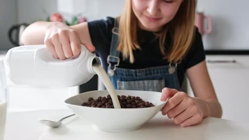 Girl Pours Milk on Chocolate Cereal for Breakfast