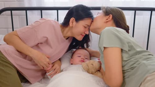 Asian lesbian couple lovingly caring for and raising their baby boy at home.