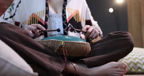 Woman playing steel tongue drum with mallets on floor at home, closeup