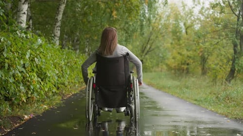 Young Woman in Wheelchair After Injury Walks in Park in Rain