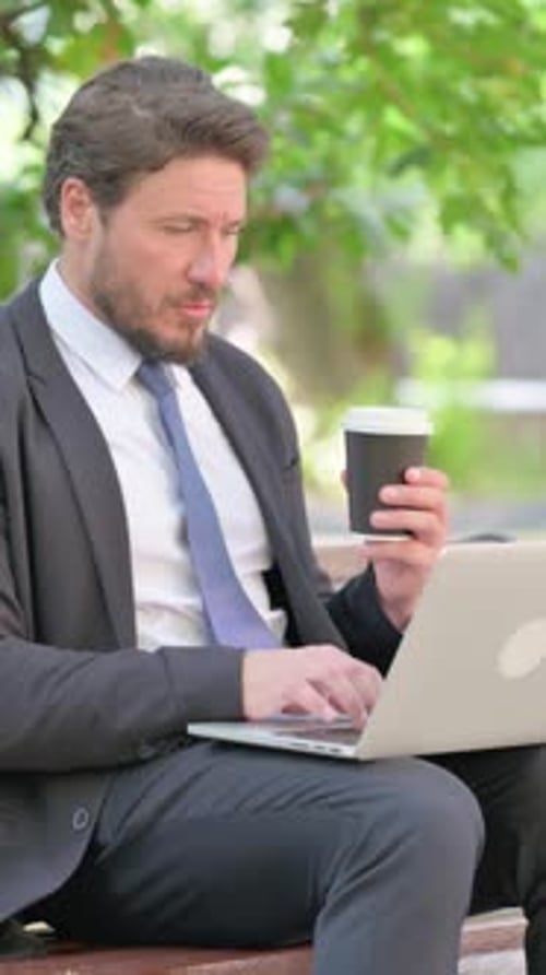 Vertical Video, Middle Aged Businessman Drinking Coffee and Using Laptop on Park Bench