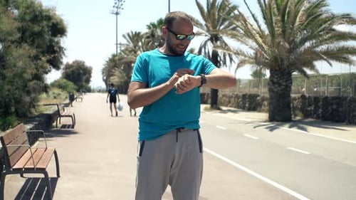 Sporty Male Jogger Checking Pulse on Smartwatch in City Park, Super Slow