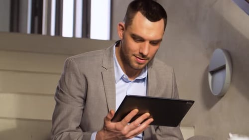 Smiling businessman with tablet pc enjoys coffee break on office stairs