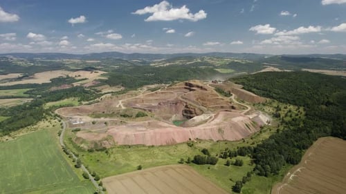Aerial orbit over the hilltop open-pit melaphyr mining quarry with heavy machinery working in the du