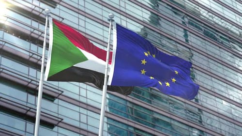 Sudan And EU Flags Waving In Wind Against Corporate Building