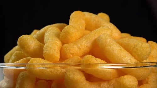 Corn cheese chips rotate in a glass bowl. Crispy cheese snack. Crispy fluffy corn sticks for break