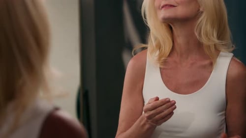 Woman Applies Lotion to Her Face in Mirror