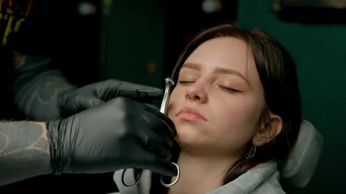 Interior de un estudio de piercings: el maestro de piercings hace un piercing para una niña, piercing para el tabique nasal