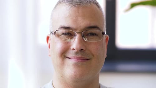 Smiling man takes off glasses, close up