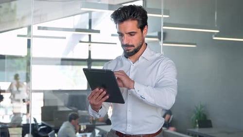 Joven empresario latino ocupado sonriente con tableta de pie en la oficina