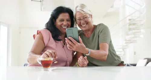 Two Smiling Women Look at Smartphone Together