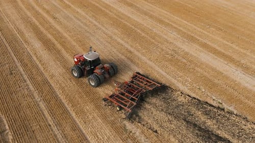 Big Red Tractor Pulling Disc Harrow Through Field in Preparation Soil for Planting New Crops