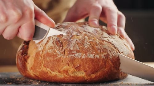 Hands Slicing Golden Loaf of Rustic Bread