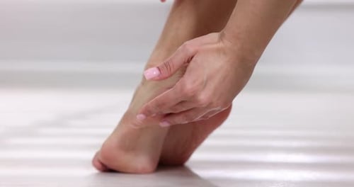 Woman applying cream on her feet indoors, closeup
