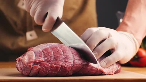 Gloved Hands Cutting Raw Beef with Knife