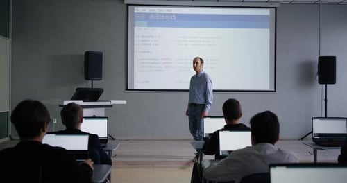 Lehrer mittleren Alters spricht im Klassenzimmer mit Schülern, Programmier- und Informatikunterricht