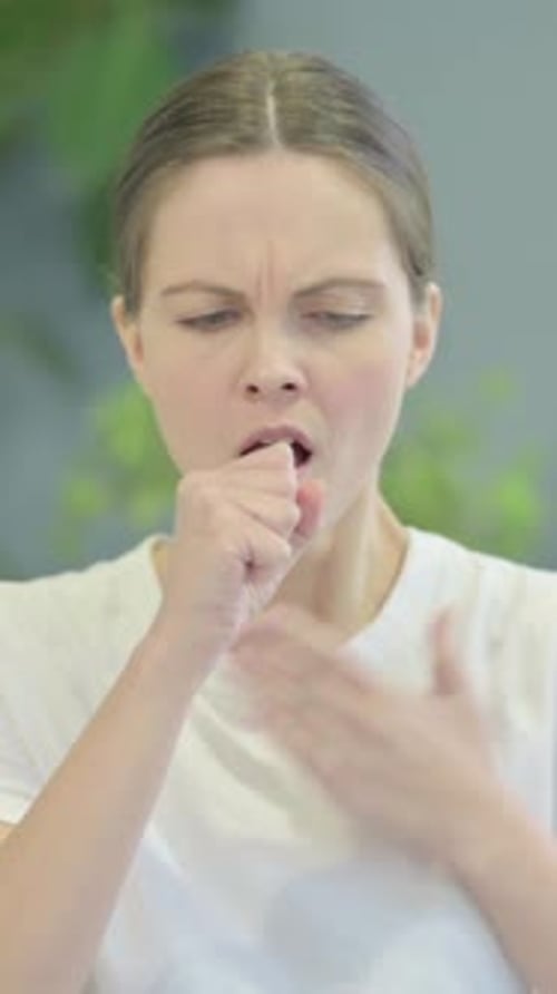 Young Woman Coughing into Her Hand Indoors