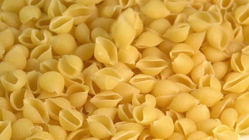 Italian pasta conchiglie rigate shell shaped falling down background closeup top view. Durum wheat