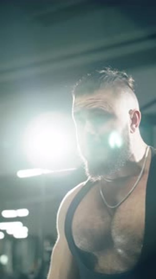 Intense Closeup of a Muscular Bearded Athlete with a Man Bun Grinding Through a Heavy Gym Workout
