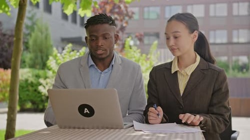 Gemischtrassige Geschäftsleute, die draußen arbeiten, schwarzer Mann und asiatische Frau benutzen gemeinsam Laptop
