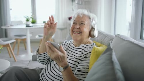 Senior Woman At Home With Smartphone And Headphones Listening To Music.