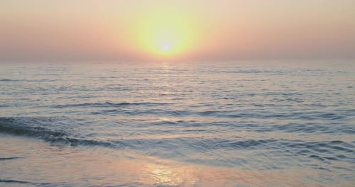 Fixed footage of a sunset at the sea in slow motion. In foreground there is the beach and some waves