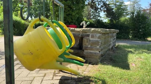 Yellow and Green Watering Cans Hanging Near a Stone Water Well