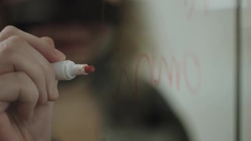 Close up of girl's hands writing on transparent glass screen with red marker, slow motion
